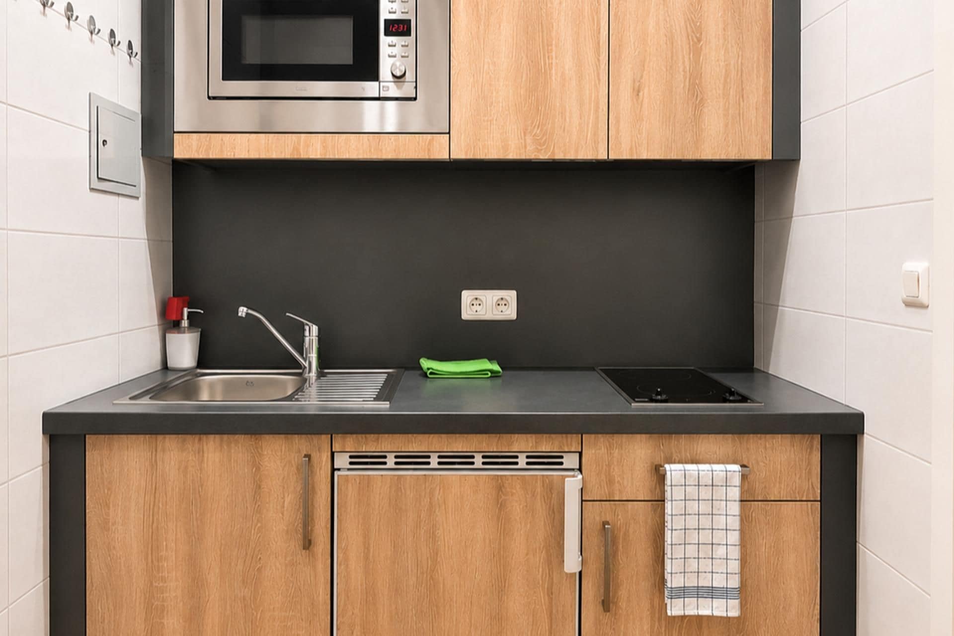 A modern kitchen with a stainless steel microwave, a sink with a faucet, a green towel, and a black stove.