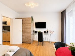 Una habitación de hotel moderna con piso de madera, un área de comedor con mesa de vidrio, un televisor de pantalla plana y una cocina con microondas.