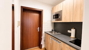 A compact kitchen with wooden cabinets, a microwave, a sink, and a dish drying rack. - City Studio Koblenz Central (Koblenz)