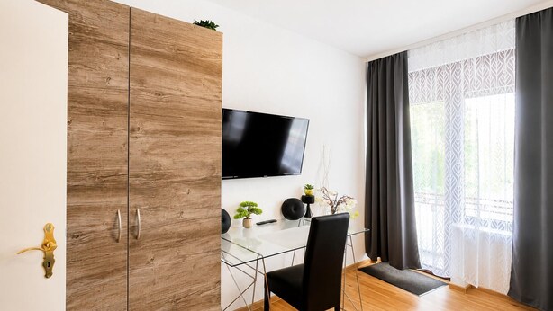 A modern room with a wooden wardrobe, a flat-screen TV, a glass dining table, and a black chair. - City Studio Koblenz Central (Koblenz)