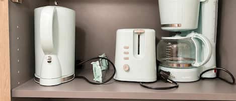 A kitchen shelf with a coffee maker, toaster, and a kettle.