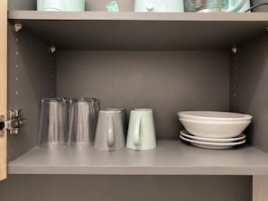 Un armario de cocina con interior gris, que contiene una pila de vasos transparentes, una taza blanca y un cuenco blanco.