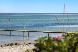 Ein Strand mit einem Kajak auf dem Wasser, einer Metallreling und etwas Vegetation im Vordergrund.