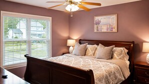A bedroom with a bed, bedside lamps, a ceiling fan, a window with blinds, and a painting on the wall. - Cozy Cottage | Close to Potomac River + Boardwalk (Colonial Beach)