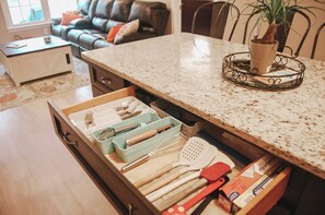 Eine Küche mit Schublade für Küchenutensilien, einer Arbeitsfläche mit Pflanze und einem Essbereich mit Sofa und Stühlen.
