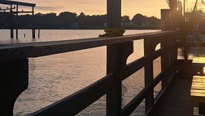 A wooden deck overlooking a body of water with a sunset in the background. - Cozy Cottage | Close to Potomac River + Boardwalk (Colonial Beach)