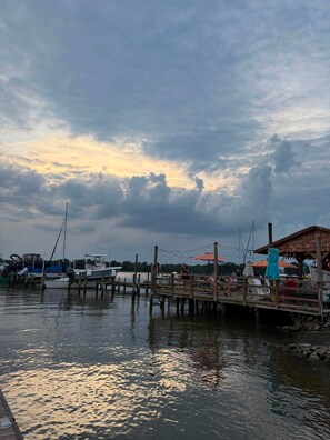 A dock with boats, a wooden pier, and a building with outdoor seating. - Cozy Cottage | Close to Potomac River + Boardwalk (Colonial Beach)