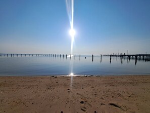 Ein Strand mit ruhiger See, einer sich ins Wasser erstreckenden Mole und der Sonne, die direkt über uns scheint.