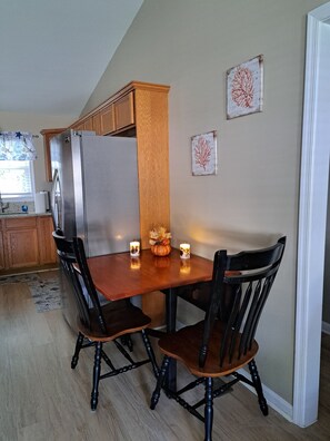 Un coin repas avec une table et des chaises en bois, un réfrigérateur et une fenêtre avec des rideaux.