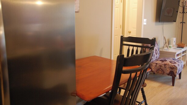 A dining area with a wooden table and chairs, a television mounted on the wall, and a door leading to another room. - Cozy Cottage | Close to Potomac River + Boardwalk (Colonial Beach)