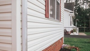 A house with a white siding exterior, a brick foundation, and a small flower bed with purple flowers. - Cozy Cottage | Close to Potomac River + Boardwalk (Colonial Beach)