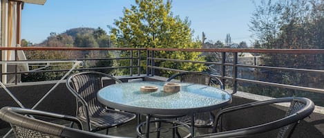 Een balkon met een ronde glazen tafel en rieten stoelen, met uitzicht op een landschap met bomen en heuvels.