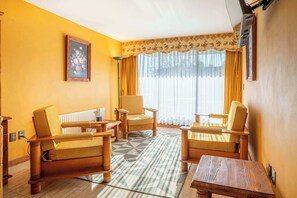Ein Wohnzimmer mit Sofa, Sesseln, einem Couchtisch, einem gemusterten Teppich und einem Bild an der Wand.