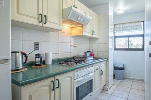 A kitchen with a gas stove, oven, and a coffee maker on the counter. - Vive Pucón: 3D/2B, Balcón y Estacionamiento (Pucon)