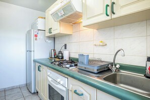 Eine kompakte Küche mit Einbauofen, Gaskochfeld, Spüle und Mikrowelle.