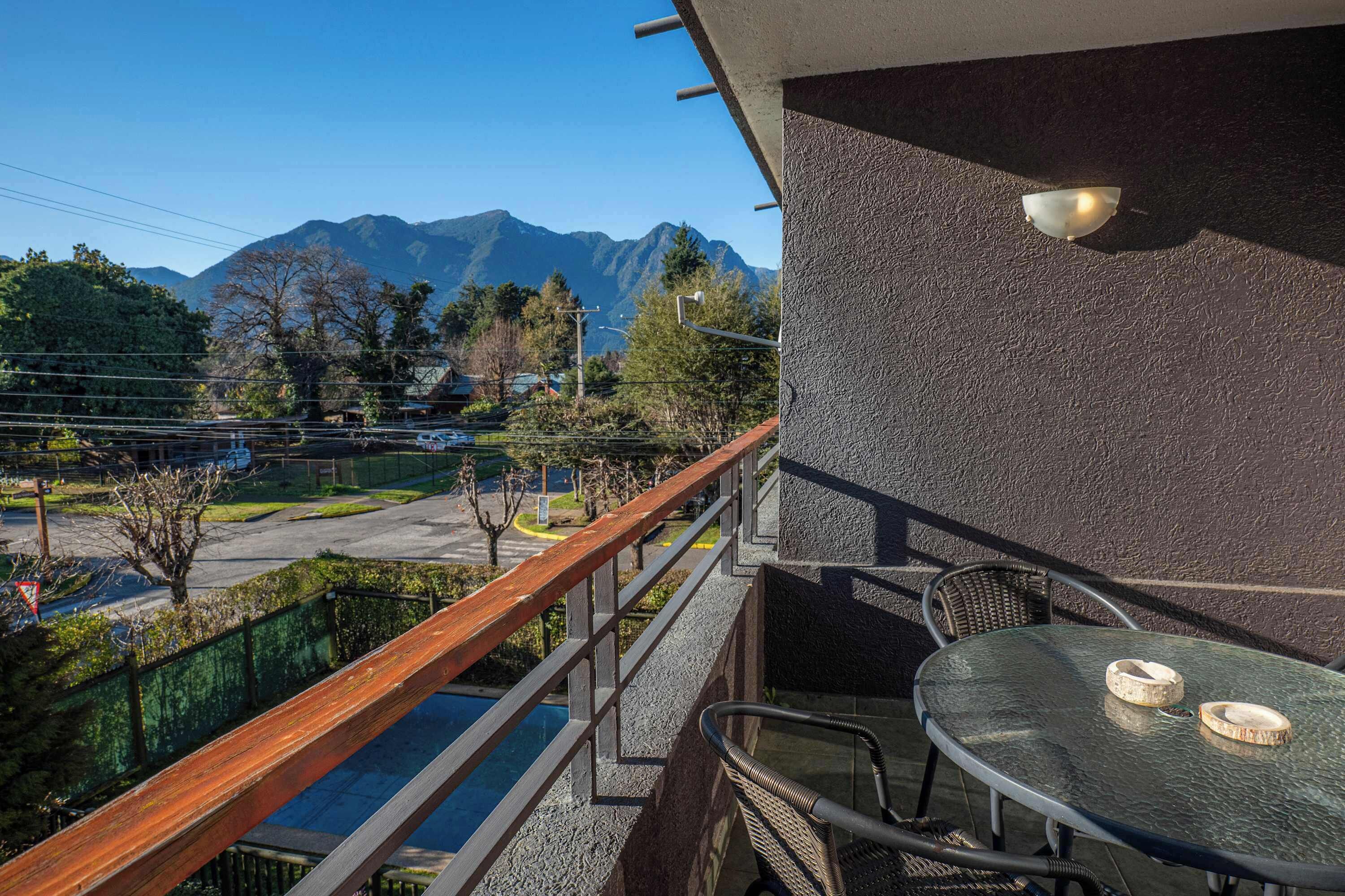 A balcony with a view of mountains, a table with chairs, and a railing.