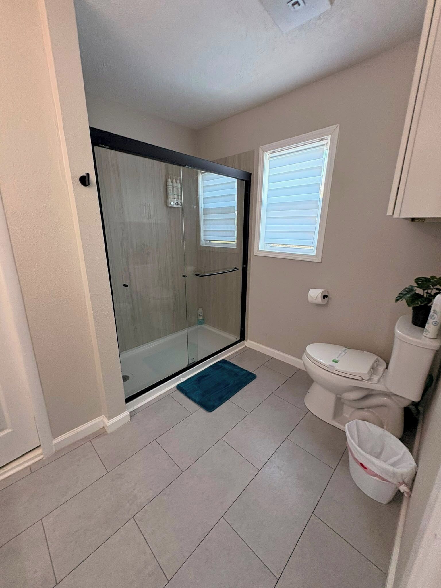 A bathroom with a glass shower enclosure, a toilet, and a small window.