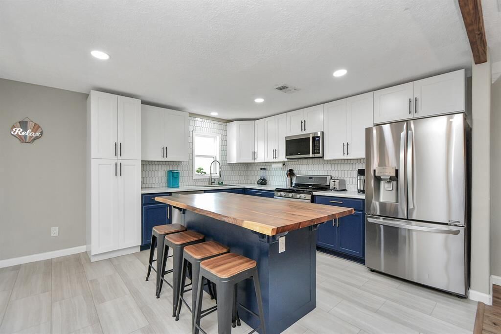 A modern kitchen with white cabinets, a stainless steel refrigerator, and a wooden island with stools.