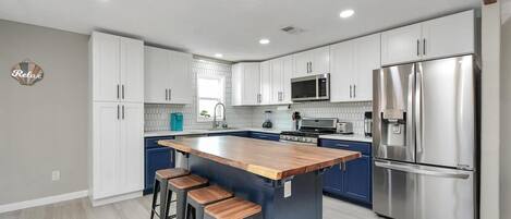 A modern kitchen with white cabinets, a stainless steel refrigerator, and a wooden island with stools.