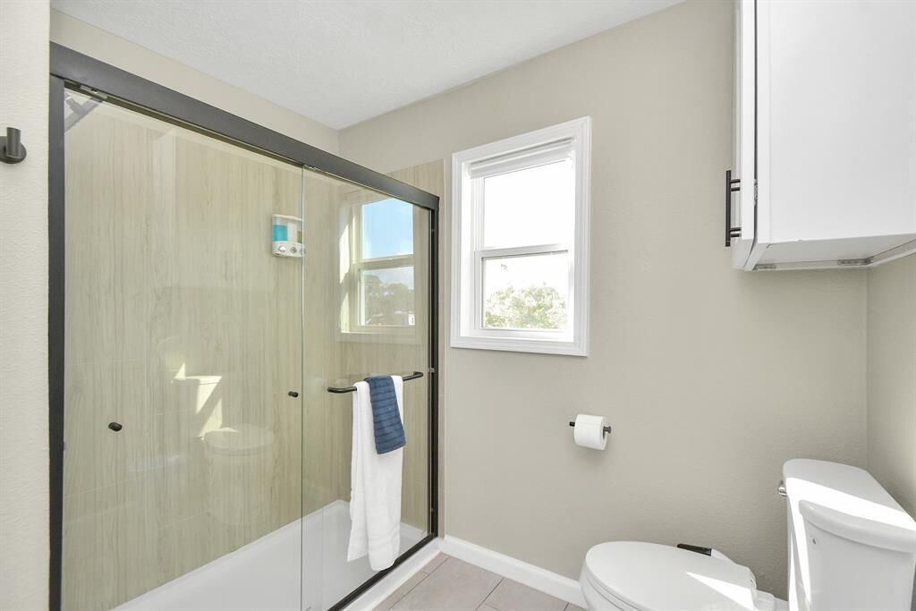 Baño con cabina de ducha de vidrio, inodoro y ventana que proporciona luz natural.
