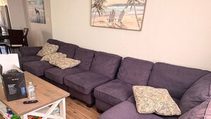 Ein Wohnzimmer mit einem Ecksofa, einem Couchtisch und einem Gemälde von einer Strandansicht.