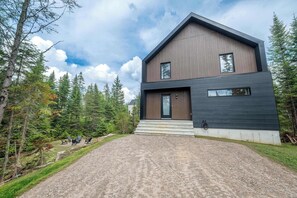 Ein modernes, zweistöckiges Haus mit Schotterauffahrt und Wald im Hintergrund.