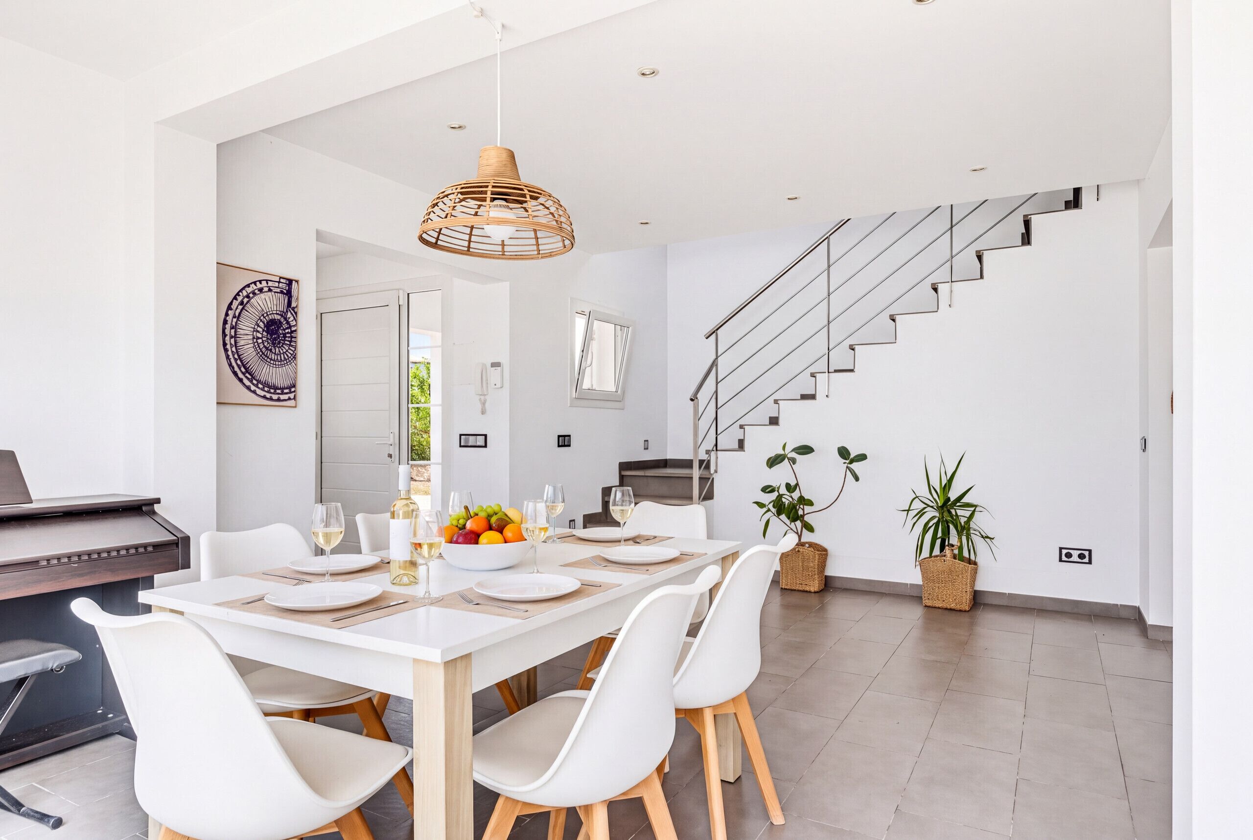 Un comedor moderno con una mesa blanca dispuesta para seis personas, rodeada de sillas blancas con patas de madera.