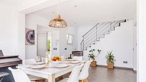 A modern dining area with a white table set for six, surrounded by white chairs with wooden legs.