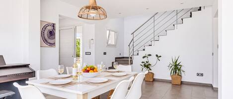 Un comedor moderno con una mesa blanca dispuesta para seis personas, rodeada de sillas blancas con patas de madera.
