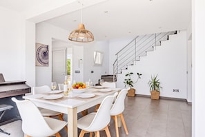 A modern dining area with a white table set for six, surrounded by white chairs with wooden legs. - Magdalena 3 bedroom villa, Cala Blanca (Cala Blanca)