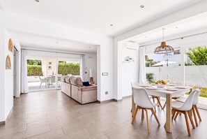 A modern interior with a dining area, a sofa, and a view of the outdoors.