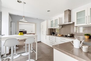 A modern kitchen with white cabinetry, a central island with bar stools, and a large window.