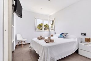 A modern bedroom with a bed, a chair, a nightstand, and a television. - Magdalena 3 bedroom villa, Cala Blanca (Cala Blanca)