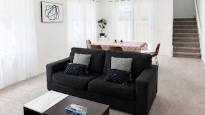 A modern living room with a dark sofa, a coffee table, and a dining area with a table and chairs.