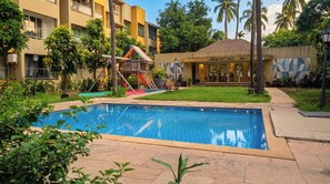 A swimming pool with a children's play area, a building with a tiled roof, and a grassy lawn. - Vibe o1: Boutique 2BHK w/pool | Just 2 mins drive to Anjuna Beach (Anjuna)