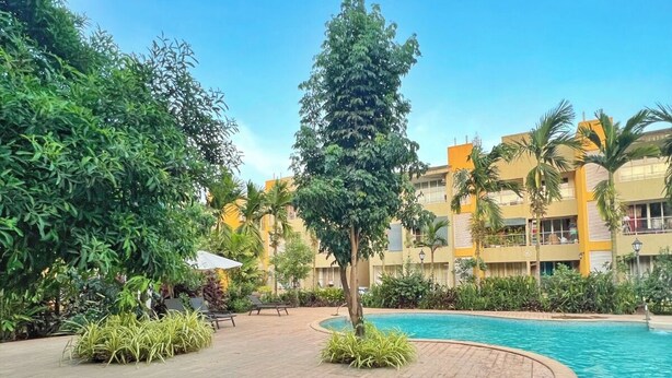 A poolside area with lounge chairs, a swimming pool, and a building with balconies in the background. - Vibe o1: Boutique 2BHK w/pool | Just 2 mins drive to Anjuna Beach (Anjuna)