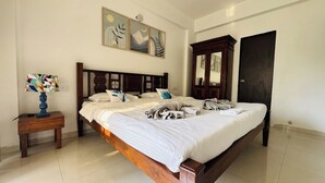 A bedroom with a wooden bed, a nightstand with a lamp, and artwork on the wall. - Vibe o1: Boutique 2BHK w/pool | Just 2 mins drive to Anjuna Beach (Anjuna)