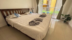 A neatly made bed with a wooden headboard, a bedside lamp, and a view of the outside balcony. - Vibe o1: Boutique 2BHK w/pool | Just 2 mins drive to Anjuna Beach (Anjuna)