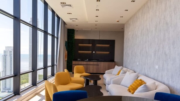 Um interior moderno com janelas amplas, um conjunto de sofás e uma área de cozinha.