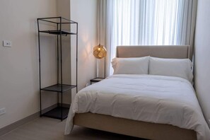Een slaapkamer met een bed, een hoog zwart metalen rek, een bedlamp en een raam met gordijnen.