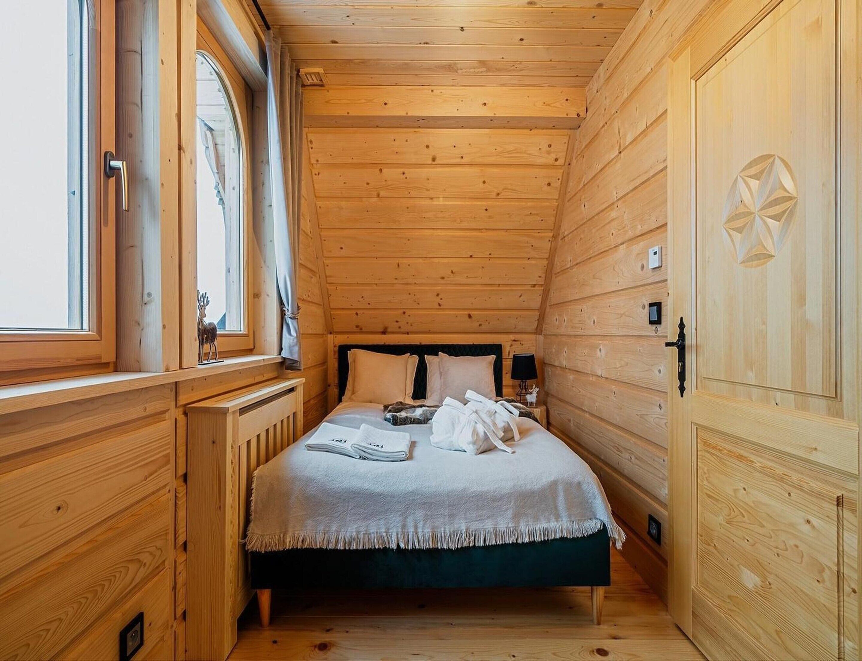 Ein Zimmer mit Holzwänden, einem Bett, einem Fenster und einer Tür.