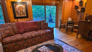 Ein gemütliches Zimmer mit einer gemusterten Couch, einem runden Couchtisch mit einer Zeitschrift und einem großen Fenster mit Blick auf Bäume.