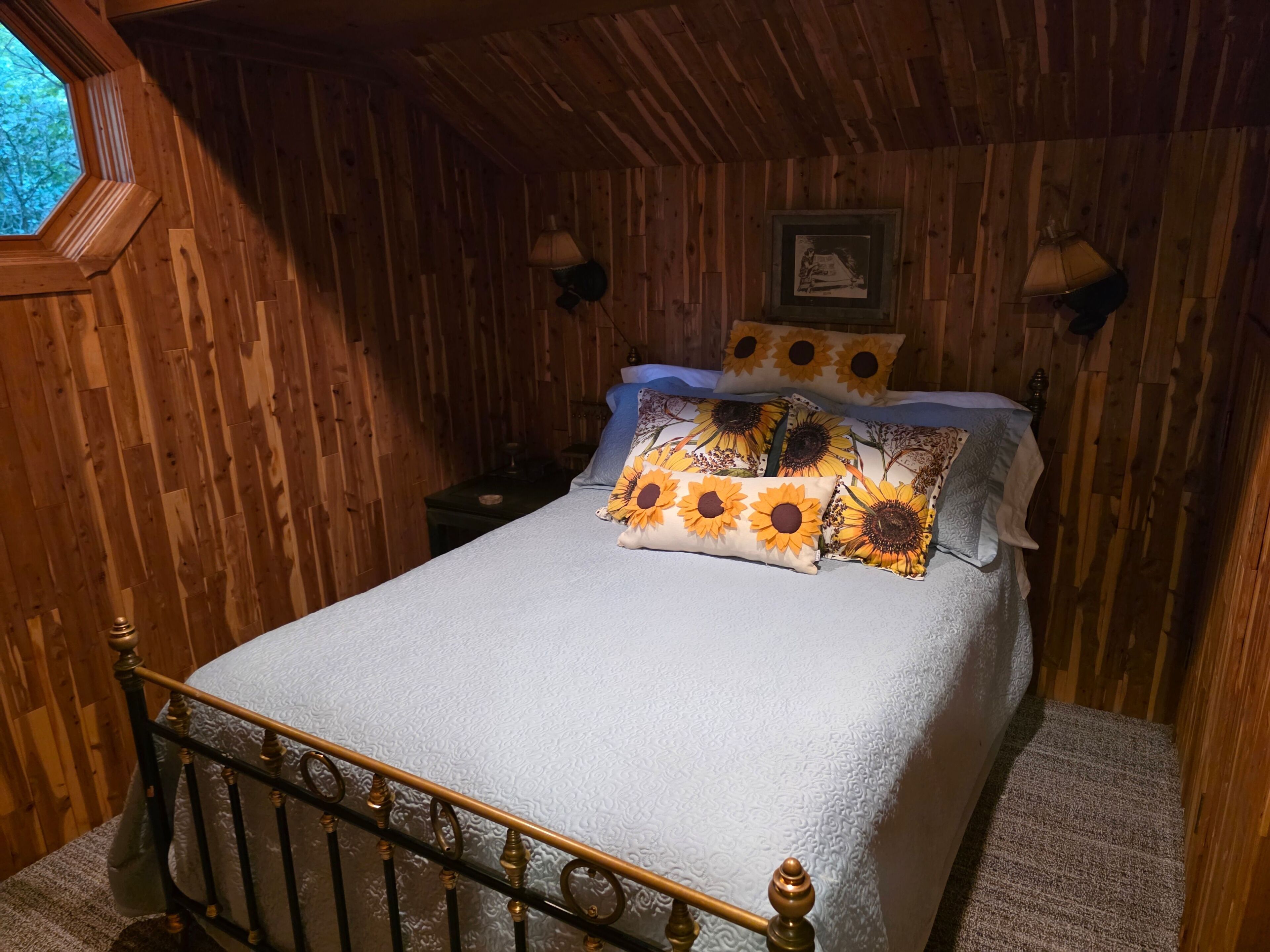 A wooden room with a bed, a window, and a wall-mounted lamp.