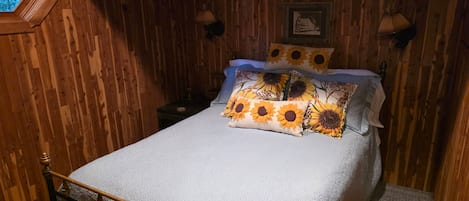 A wooden room with a bed, a window, and a wall-mounted lamp.