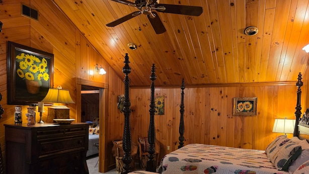 Ein Schlafzimmer mit Holzwandverkleidung, einem Himmelbett, einem Schminktisch und einem Deckenventilator.