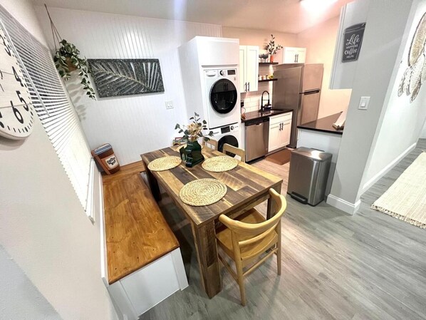 A compact kitchen with a wooden dining table, built-in appliances, and a clock on the wall.