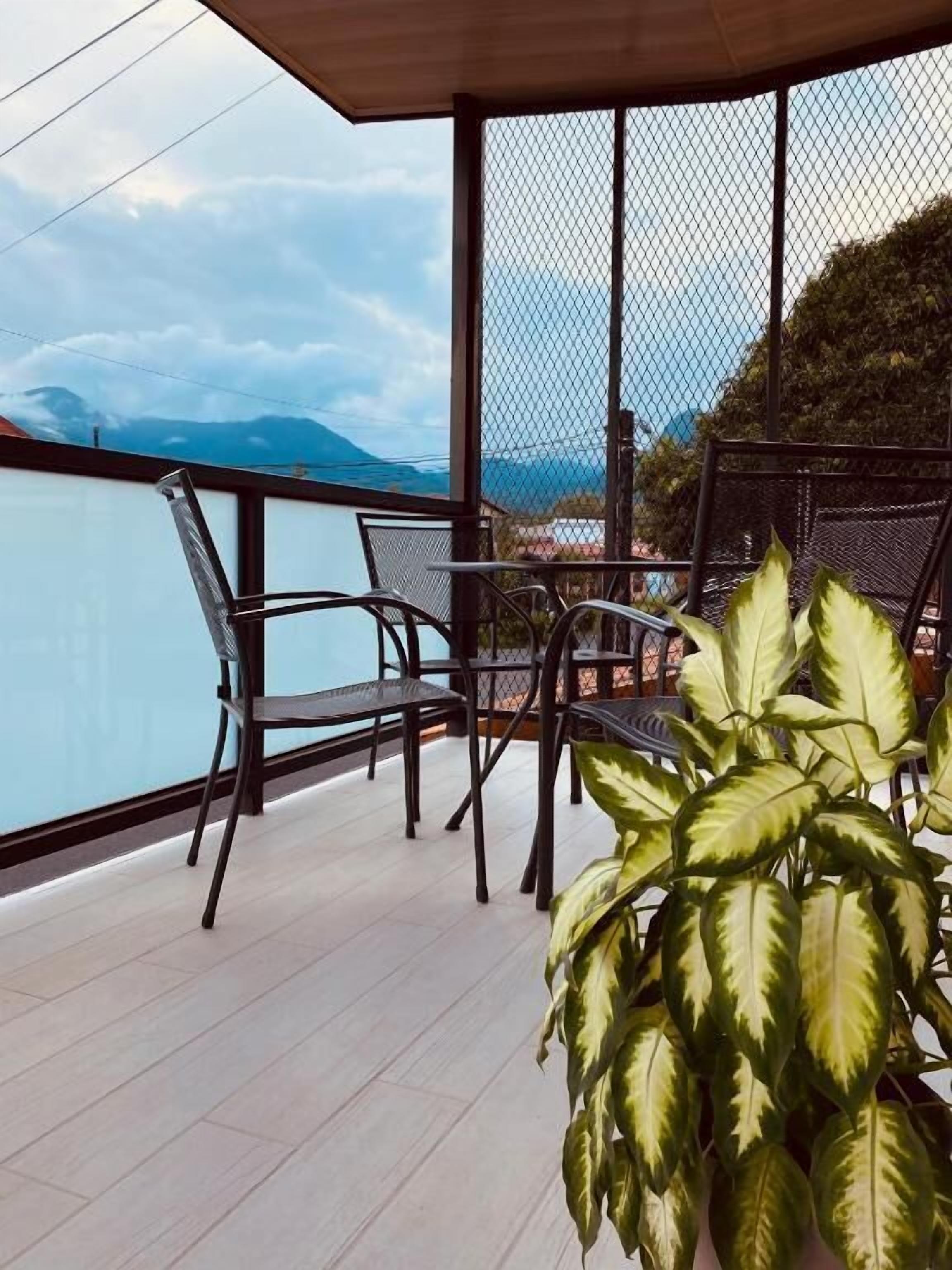 A balcony with a view of the sea and mountains, featuring a table and chairs.