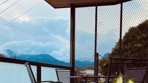A balcony with a view of the sea and mountains, featuring a table and chairs.