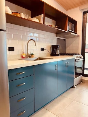 A kitchen with a white countertop, blue cabinets, a stainless steel sink, and a stove.
