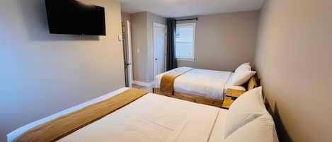 A bedroom with two beds, a television mounted on the wall, and a ceiling light fixture.
